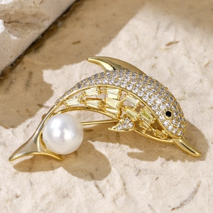 Detail shot of golden dolphin brooch with cubic zirconia stones and round white pearl