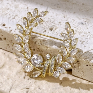 Close-up of golden laurel leaf brooch with sparkling zircons on a stone background