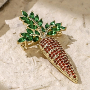 Detailed view of carrot-shaped brooch featuring green and orange stones in gold plating
