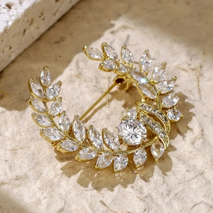 Elegant gold wheat brooch with marquise zirconia crystals on warm textured stone background