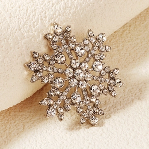 Macro shot of silver snowflake brooch with sparkling crystal inlay on a textured background