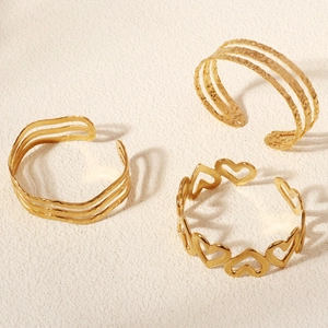 Detailed view of three-piece gold metal bangle set with wavy texture and open heart patterns