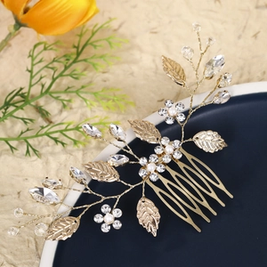 Detail of bridal hair comb featuring pearls, crystals, and gold metal leaves on a tray