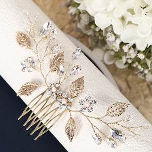 Close-up of golden bridal hair comb with leaf motifs, white pearls, and sparkling crystals