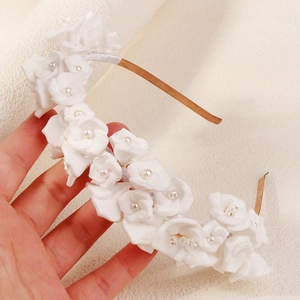 Detail view of handmade white clay flowers and pearls on a bridal gold metal headband