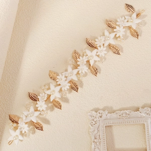 Detailed close-up of white clay flowers and gold leaves on an elegant bridal headband