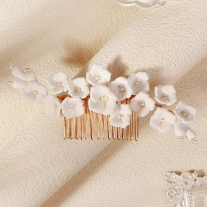 Close-up of handmade white clay flowers and pearls on a gold bridal hair comb