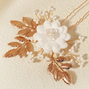 Elegant gold leaf bridal hair pin with white flowers and pearls on a beige background