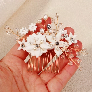 Close-up of handmade bridal hair comb with white clay flowers and pearls on gold metal pins