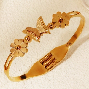 Dettaglio di bracciale dorato a molla con farfalla opaca e ciondoli a forma di fiori
