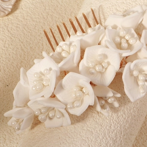 Close-up of white floral hair comb with delicate resin petals and pearls on gold base