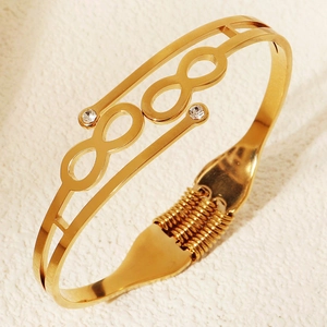 Dettaglio di un bracciale dorato a molla con doppi simboli dell'infinito e cristalli