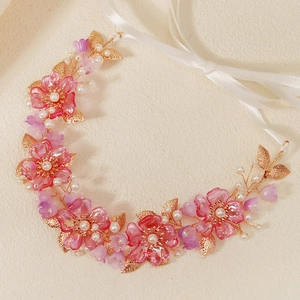Close-up of pink resin flowers, white pearls and gold metal leaves on a bridal headband