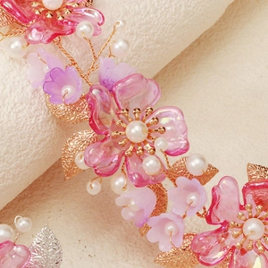 Close-up of pink resin flowers, gold metal leaves and white pearls on bridal headband