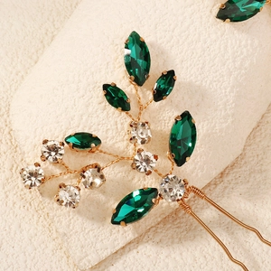 Close-up of golden wired leaf hair pins with emerald marquise and clear crystals