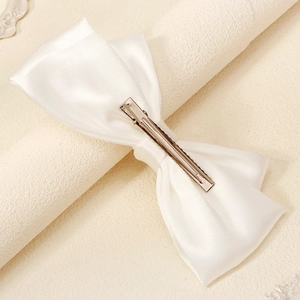 Détail du nœud de mariée en satin blanc avec pince crocodile en métal pour cheveux chic