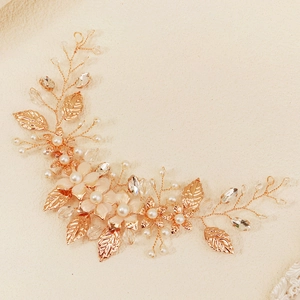 Handmade bridal hairpiece with rose gold beads and petals on a sandy texture background