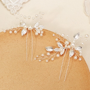 Elegant bridal hair pins with silver metal leaves and pearls on a textured background