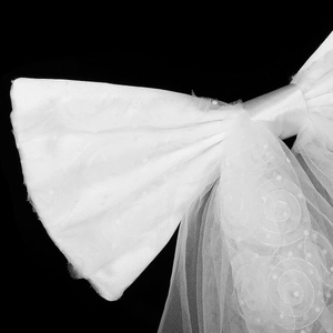 Detail of white bridal bow hair clip featuring embroidered rose lace and elegant pearls