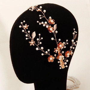 Detail van roségouden bruidshaarstuk met metalen bloemen en witte parels op zachte ketting