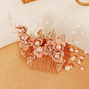 Macro detail van bruidshaarkam met roze stoffen bloemen en goudkleurige metalen bladeren