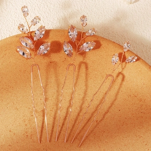 Dettaglio di tre forcine da sposa dorate con cristalli marquise a foglia su vassoio arancione