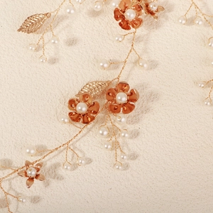 Detail van handgemaakte bruidshaarband met gouden bloemen, bladeren en witte parels