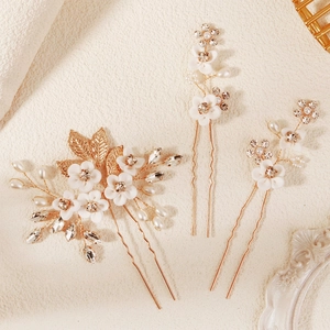 Detailed close-up of bridal hairpins with white ceramic flowers, pearls, and gold leaves