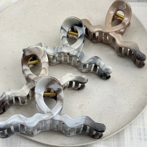 Close-up of four wavy claw clips with marble and leopard patterns on a ceramic tray