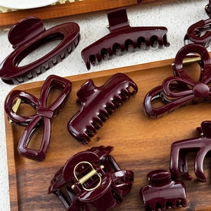 Set of elegant burgundy hair clips and claws on dark wood tray with gold springs