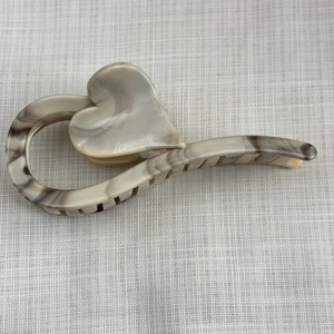 Macro shot of large marble ink heart hair claw clip on neutral textured fabric background