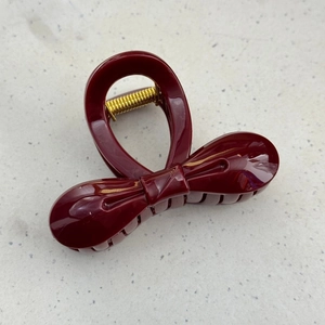 Macro detail of wine red bow hair claw clip showing polished finish and golden metal spring