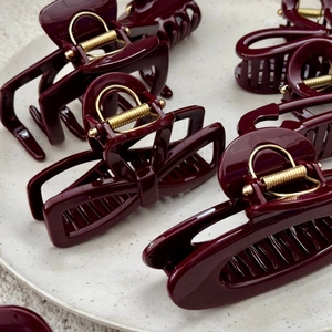 Elegant burgundy hair claw clips with gold metal spring on a ceramic display tray