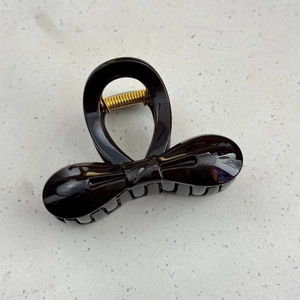 Detail of dark brown bow hair claw clip with golden metal spring on grey surface