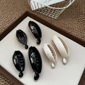 Three glossy banana hair clips in black, coffee, and cream white displayed in a wooden tray