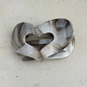 Detail view of heart-shaped hair claw with grey marble pattern and golden metal spring