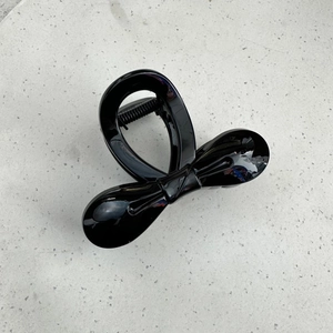 Detail showing the glossy black bow hair claw clip with strong metal spring and mirror finish
