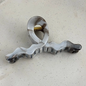 Macro shot of marble textured hair claw clip with wave design and gold metal spring