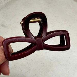 Detail of burgundy bow hair claw clip showing polished finish and gold spring mechanism