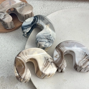 Detailed set of four marbled resin hair claws in neutral tones on decorative trays