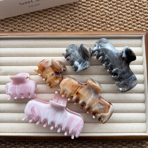 Set of six marble texture hair claws in pink, amber, and grey on a beige velvet tray