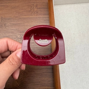 Close-up of a burgundy hair claw clip with fine glitter finish and gold logo text