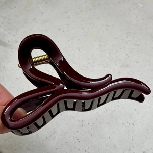 Detail of burgundy hair claw clip with a glossy finish and premium gold spring