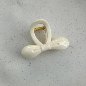 Detail of a creamy white bow hair claw clip with golden metal spring on stone surface