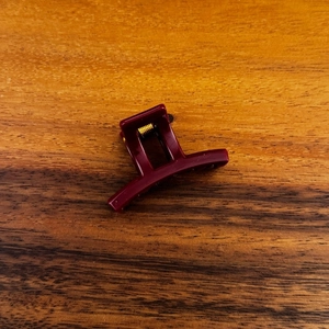 Detailweergave van een wijnrode kleine haarklem met een gouden metalen veer op hout