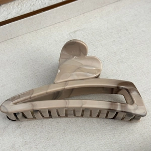 Detail of heart-shaped hair claw with brown marble ink pattern on soft grey fabric