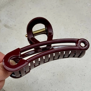 Detail of burgundy safety pin hair claw clip with gold spring and glossy finish