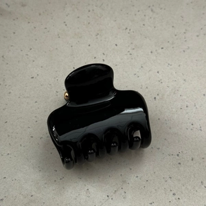 Close-up of a glossy black hair claw clip with golden metal spring on a stone surface