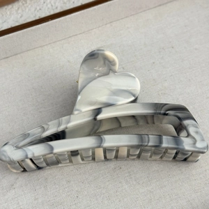 Macro shot of marble texture hair claw clip with heart detail on beige fabric background