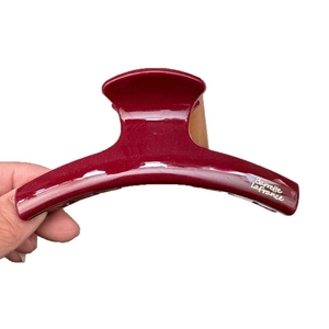 Glossy deep red hair claw clip with gold lettering held by a hand on a white background